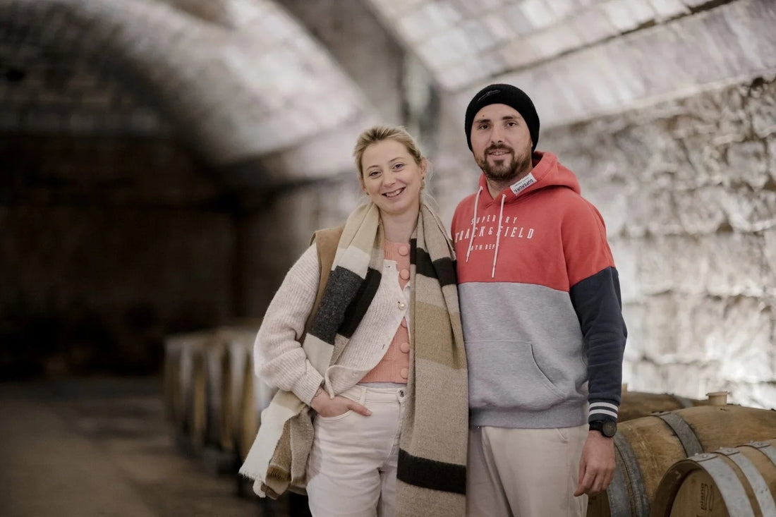 Smiling couple in casual clothing standing in a wine cellar with wooden wine barrels