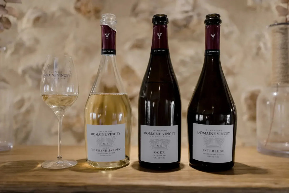 Domaine Vincey champagne bottles and wine glass on wooden table with stone wall backdrop