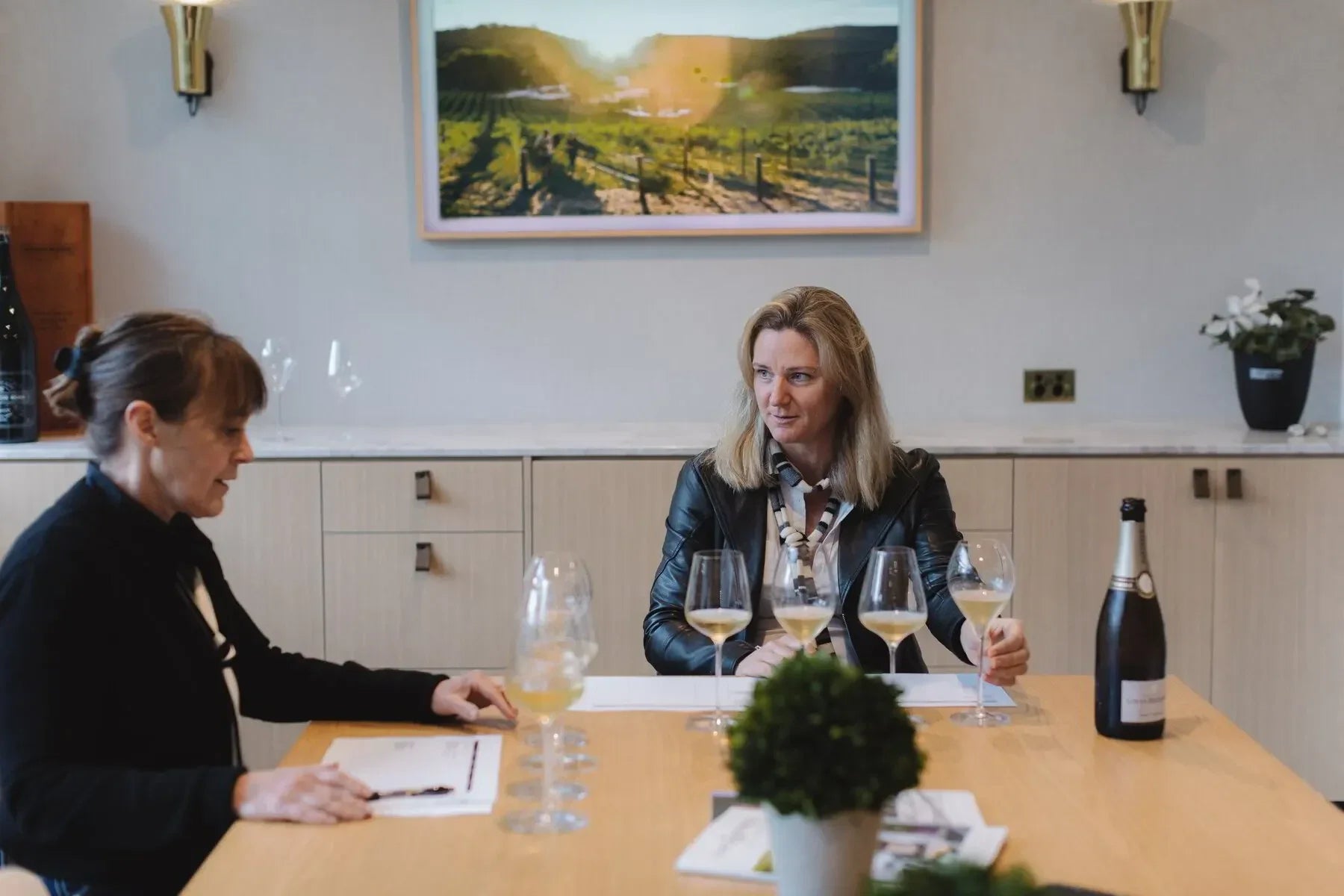 Two women wine tasting at a modern table with glasses and a champagne bottle