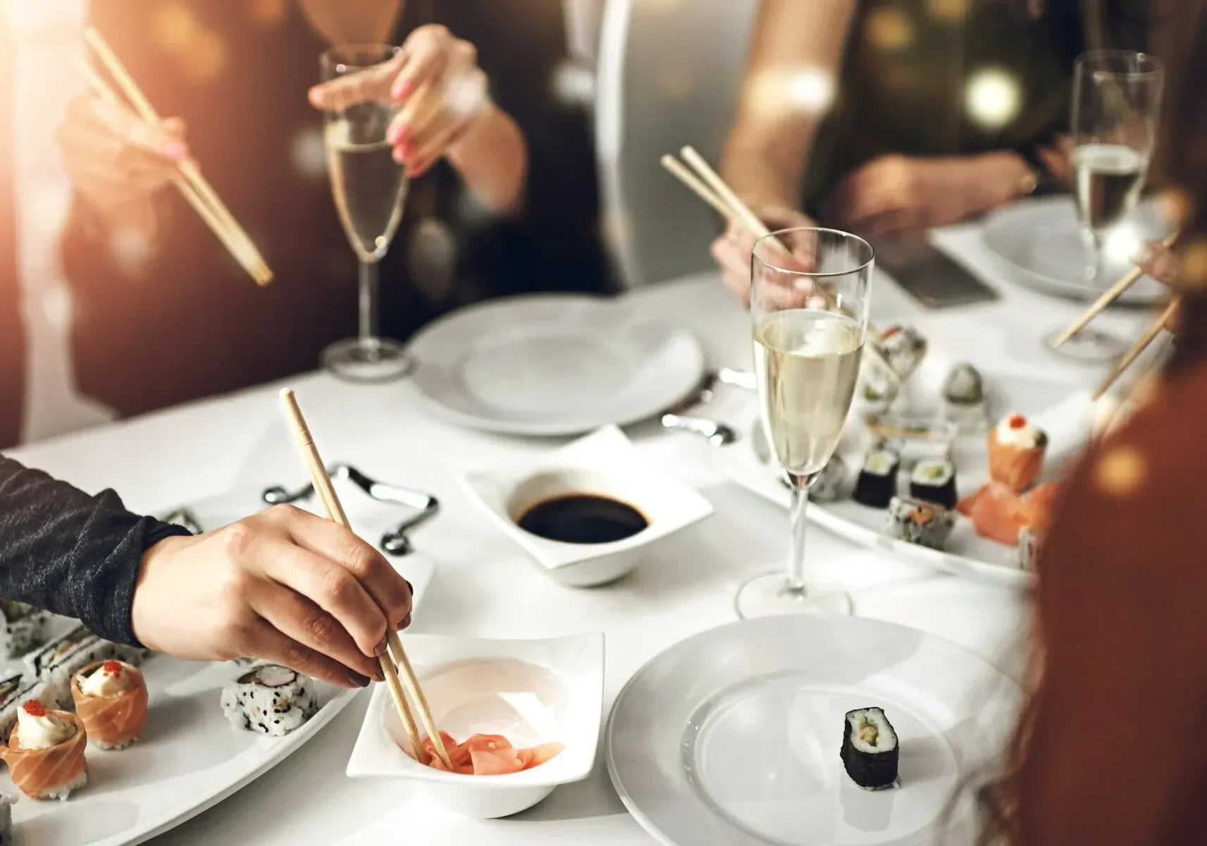 Sushi and champagne pairing on a white table, people using chopsticks and flutes