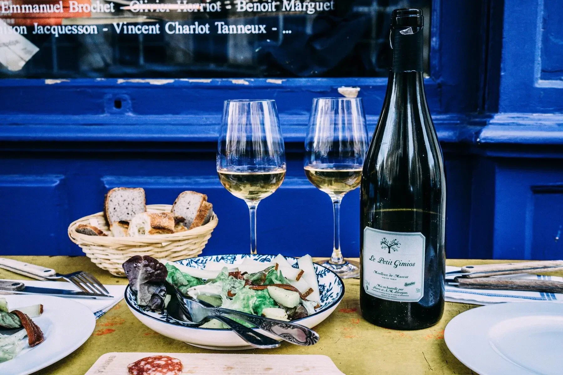 French bistro table with salad, bread, white wine, and Le Petit Gimios bottle