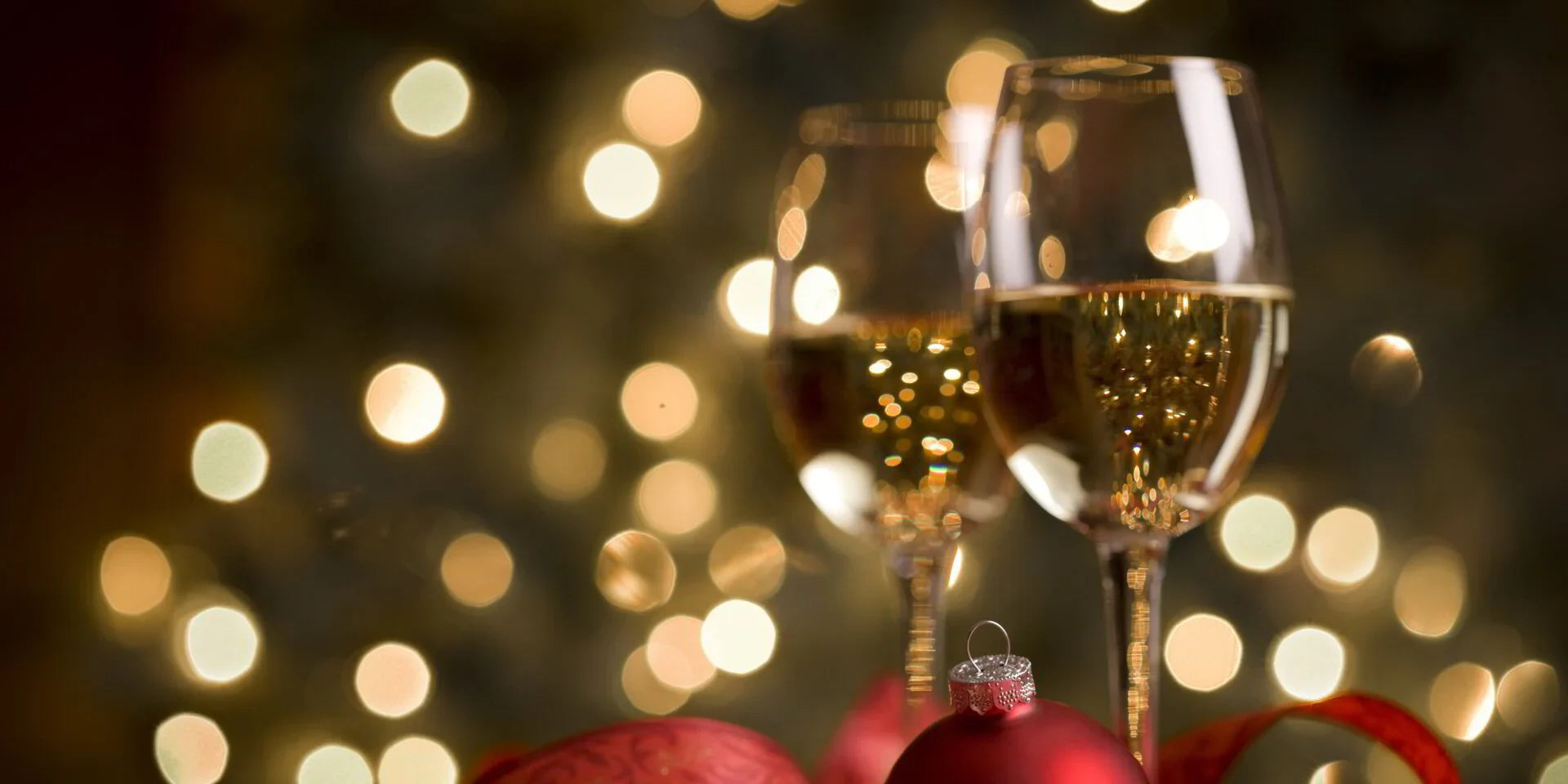 Two champagne glasses with Christmas ornaments and festive lights background