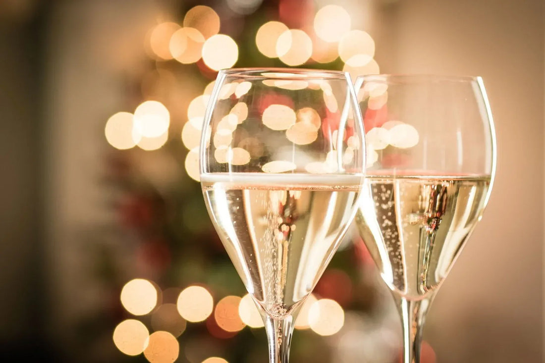 Two champagne glasses with sparkling wine, Christmas tree lights blurred in background