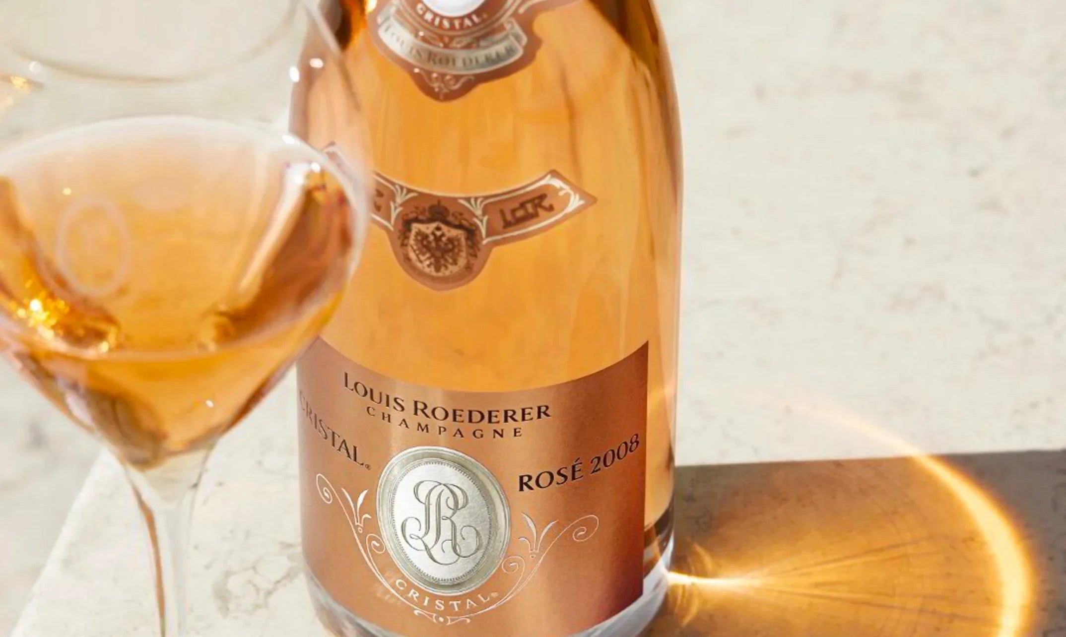 Louis Roederer Cristal Rosé 2008 champagne bottle and glass on a light marble surface