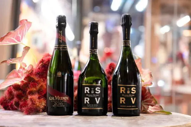 Three GH Mumm champagne bottles displayed on a table with decorative flowers