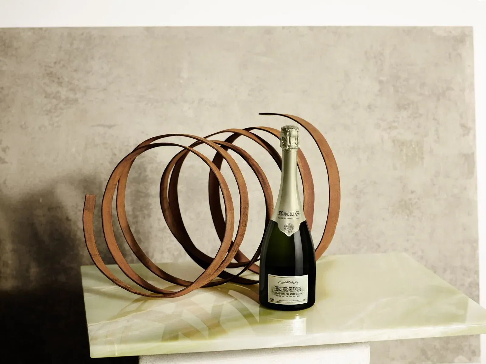 Krug Clos du Mesnil 2009 champagne bottle on marble table with abstract metal sculpture