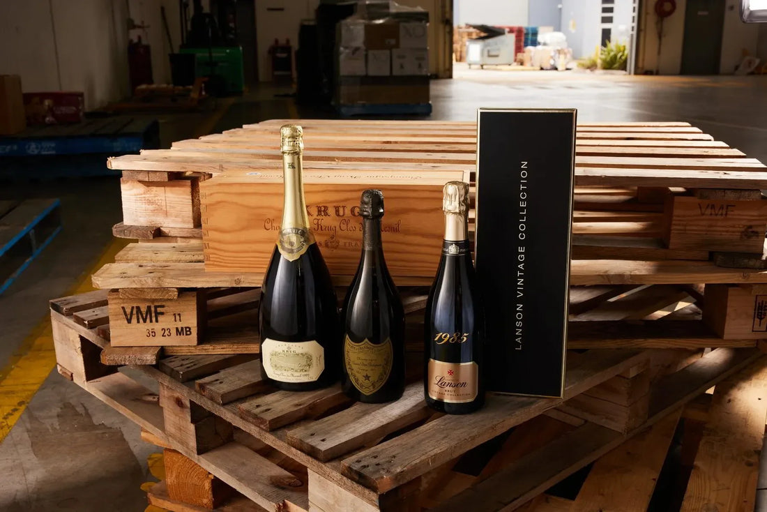 Vintage champagne bottles and Lanson Vintage Collection box on wooden pallets in a warehouse.