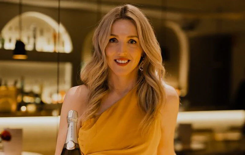 Woman in a gold dress holding a Louis Roederer champagne bottle in a stylish bar
