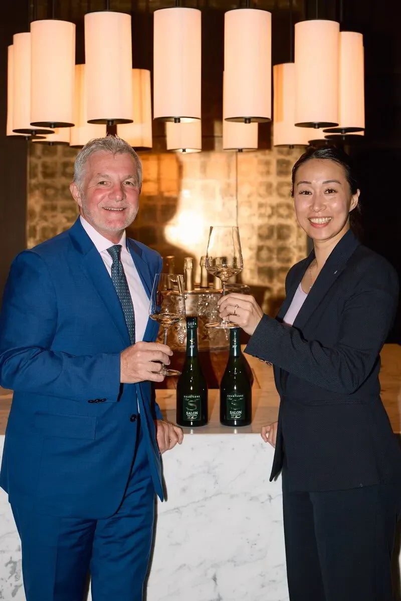 Two people in suits toasting champagne at a luxury bar with Salon bottles and modern lights