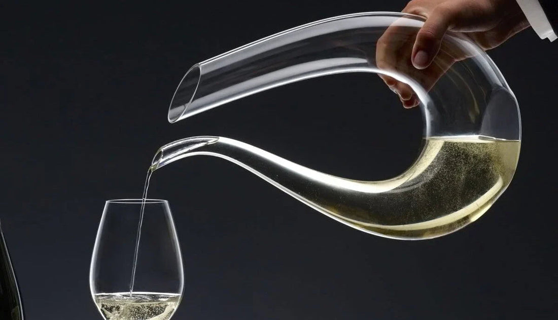 Hand pouring champagne from Riedel decanter into glass against dark background