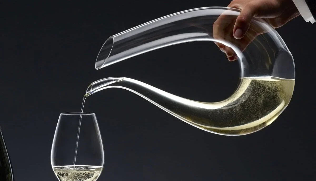 Hand pouring champagne from Riedel decanter into glass against dark background