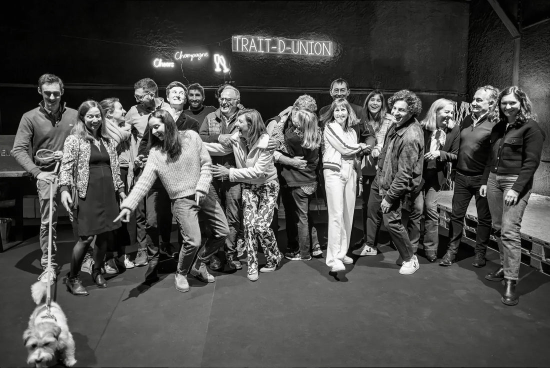 Group of people with a dog in front of a neon TRAIT-D-UNION Champagne sign