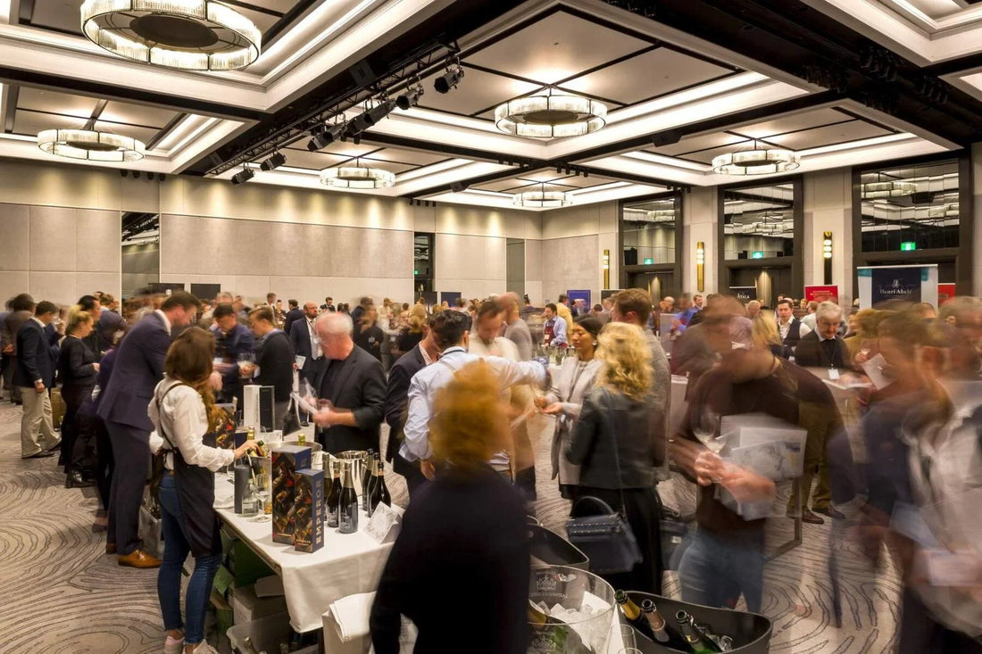 Crowded champagne tasting event in a modern banquet hall with bottles on tables