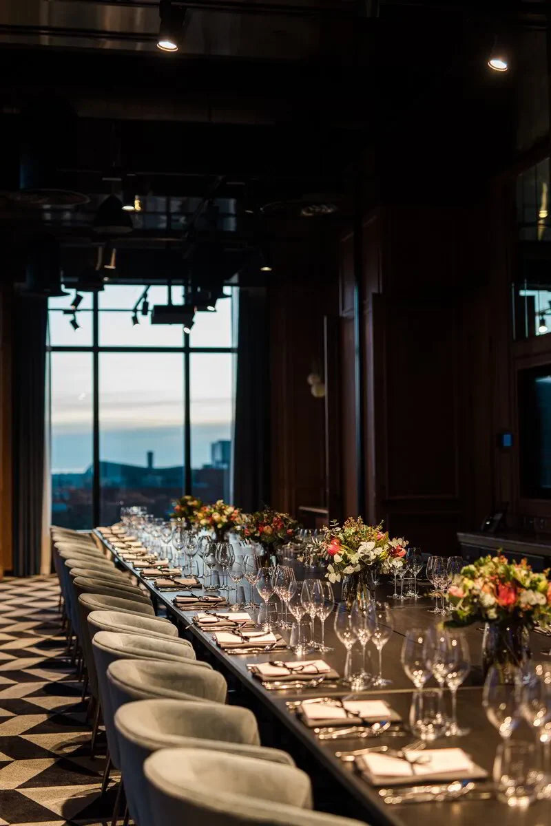 Elegant dining room with long table, modern chairs, floral centerpieces, and city view