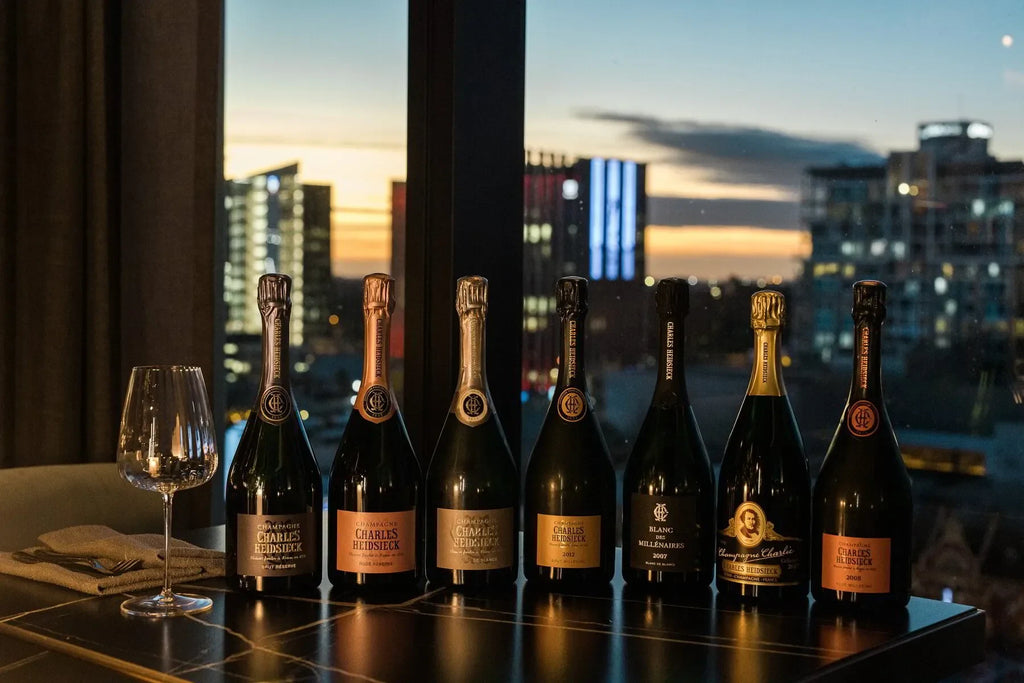 Charles Heidsieck champagne bottles lined up on a table with wine glass at sunset city view