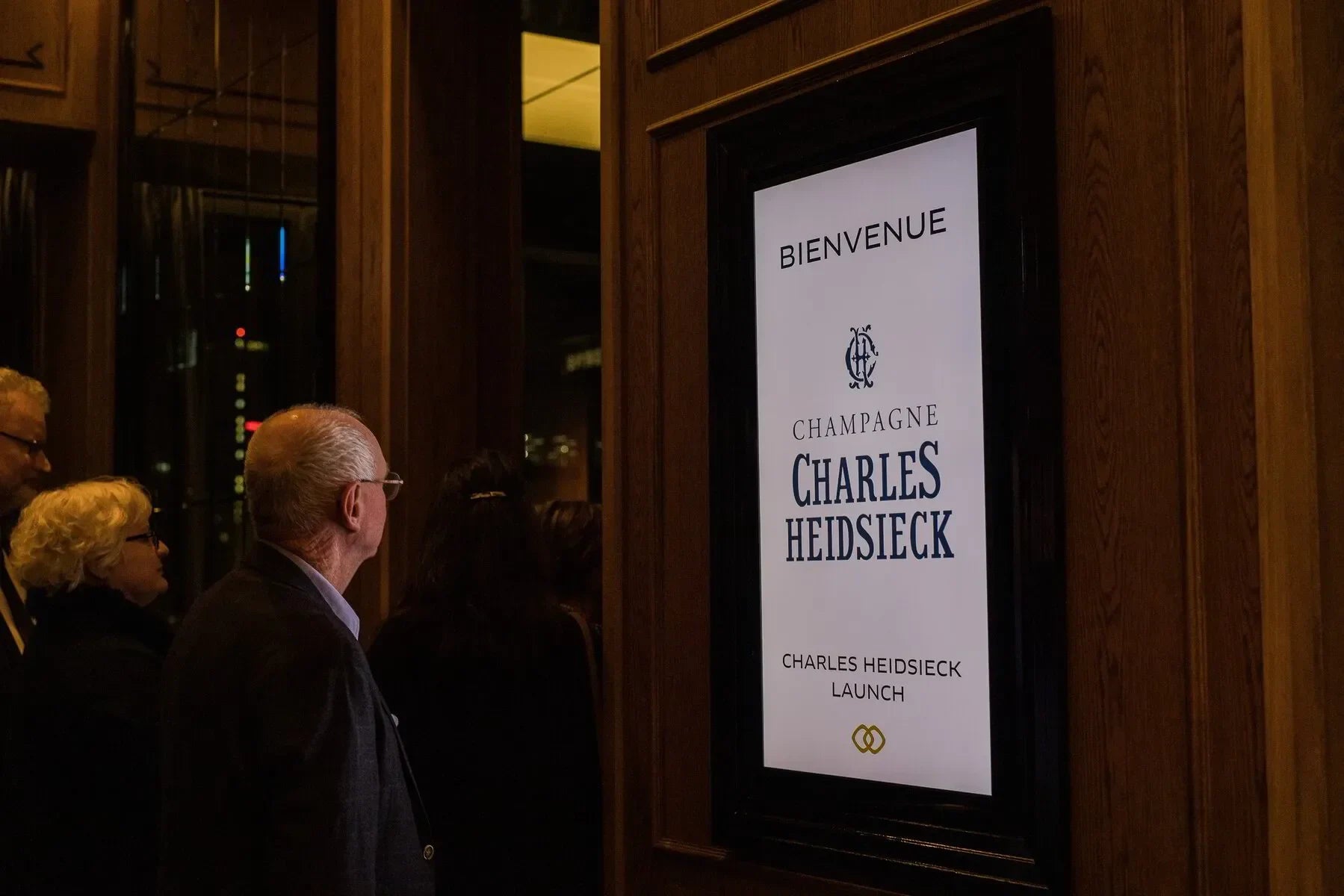 People viewing digital sign for Champagne Charles Heidsieck launch event in upscale venue