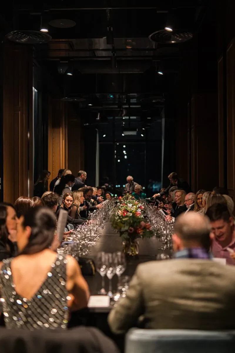 Elegant dinner party with guests seated at long banquet table with floral centerpiece