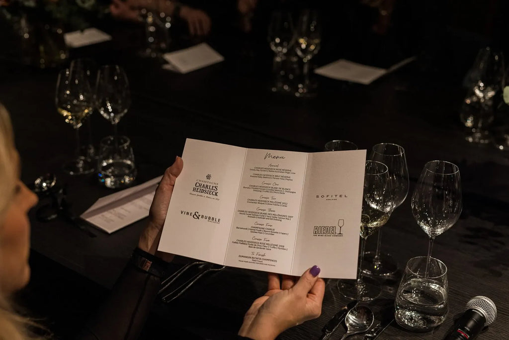 Woman holding a champagne tasting menu at a formal dinner table with wine glasses