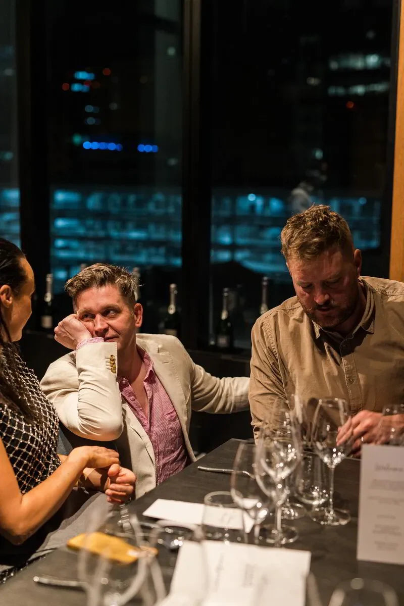 Three adults at an elegant dinner table with wine glasses in a city restaurant at night