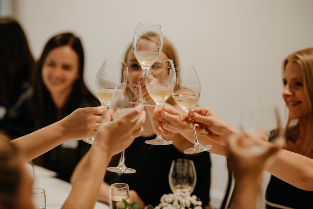 Group of people raising champagne glasses for a toast during a social gathering with soft indoor lighting