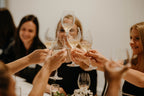 Group of people raising champagne glasses for a toast during a social gathering with soft indoor lighting