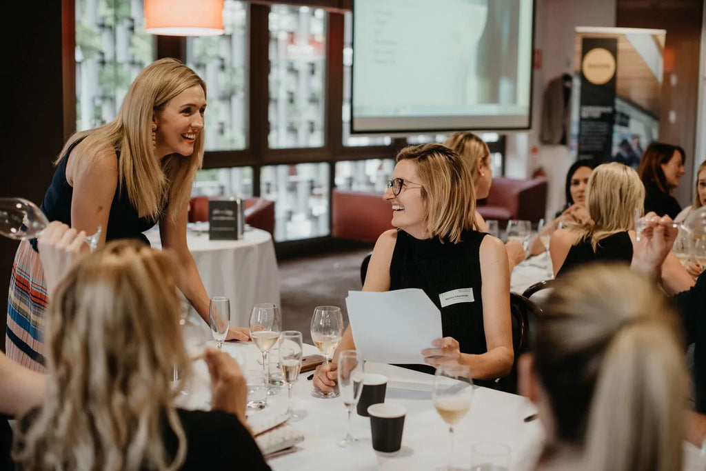 Women networking at business event with wine glasses and presentation screen