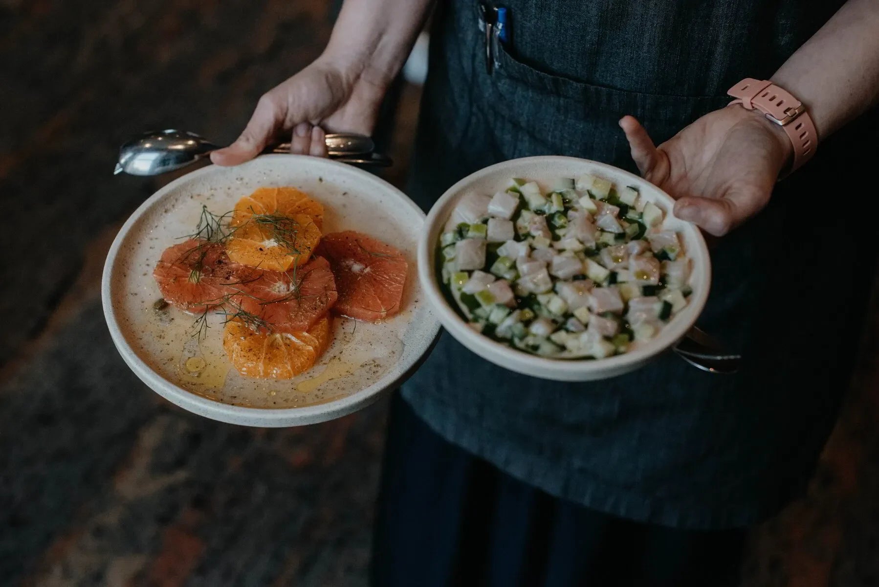 Person in apron holding citrus salad and diced fish ceviche in ceramic bowls