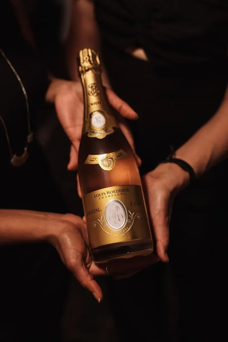 Hands holding a Louis Roederer Cristal Champagne bottle in a dimly lit setting