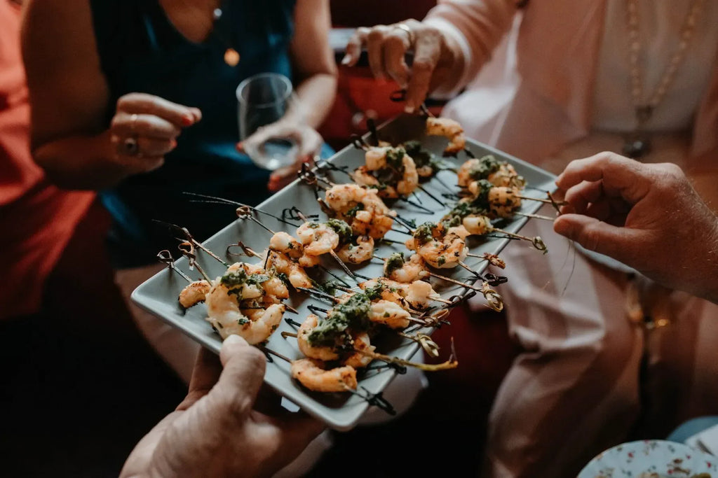 People sharing grilled shrimp skewers appetizer at a party, gourmet seafood platter