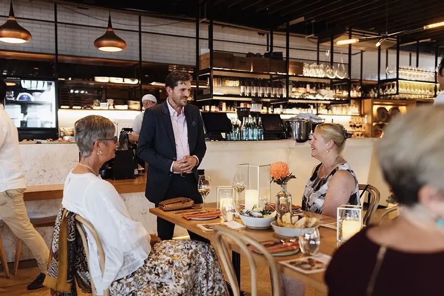 Restaurant event with people dining, man in suit talking, appetizers and wine on table
