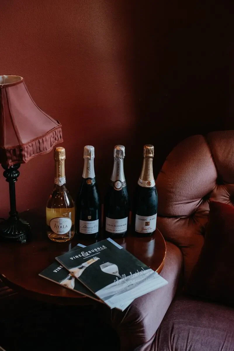 Four champagne bottles and Vine & Bubble magazines on a wooden table in a cozy lounge setting.