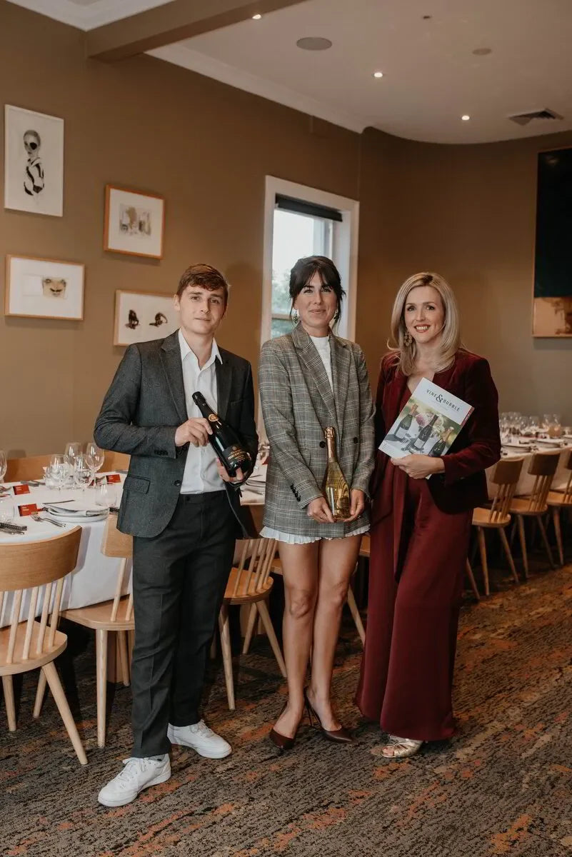 Three people dressed smartly holding champagne and a magazine at an elegant restaurant event