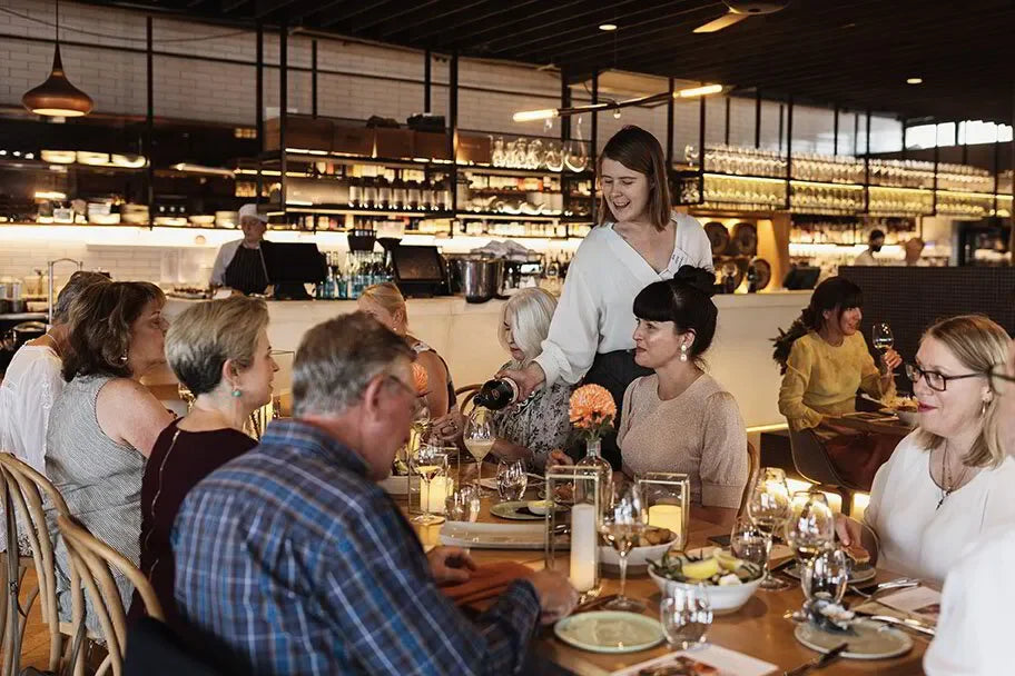 Group dining in modern restaurant with server pouring wine at lively dinner event