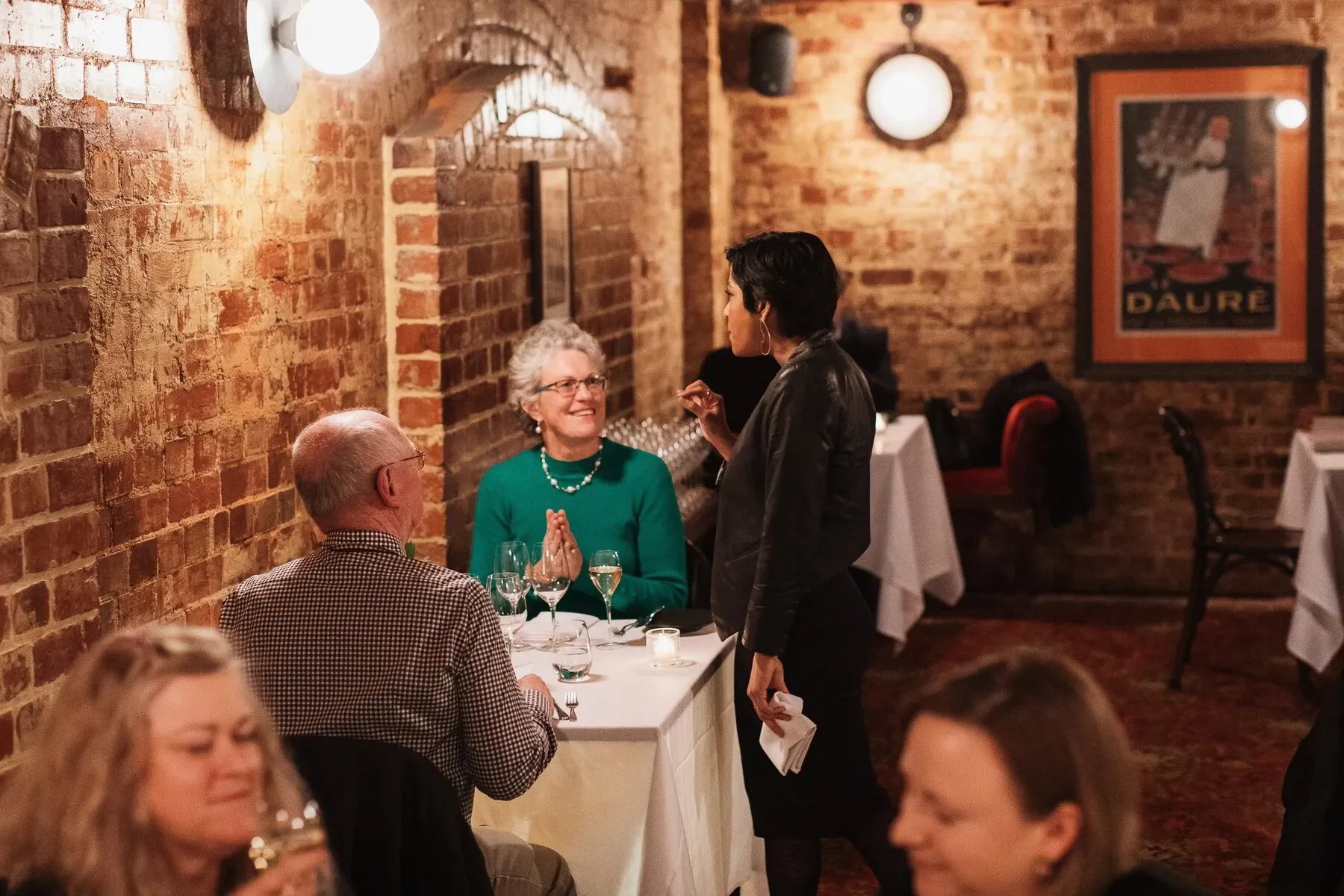 People dining in a cozy brick-walled restaurant with white tablecloths and wine glasses
