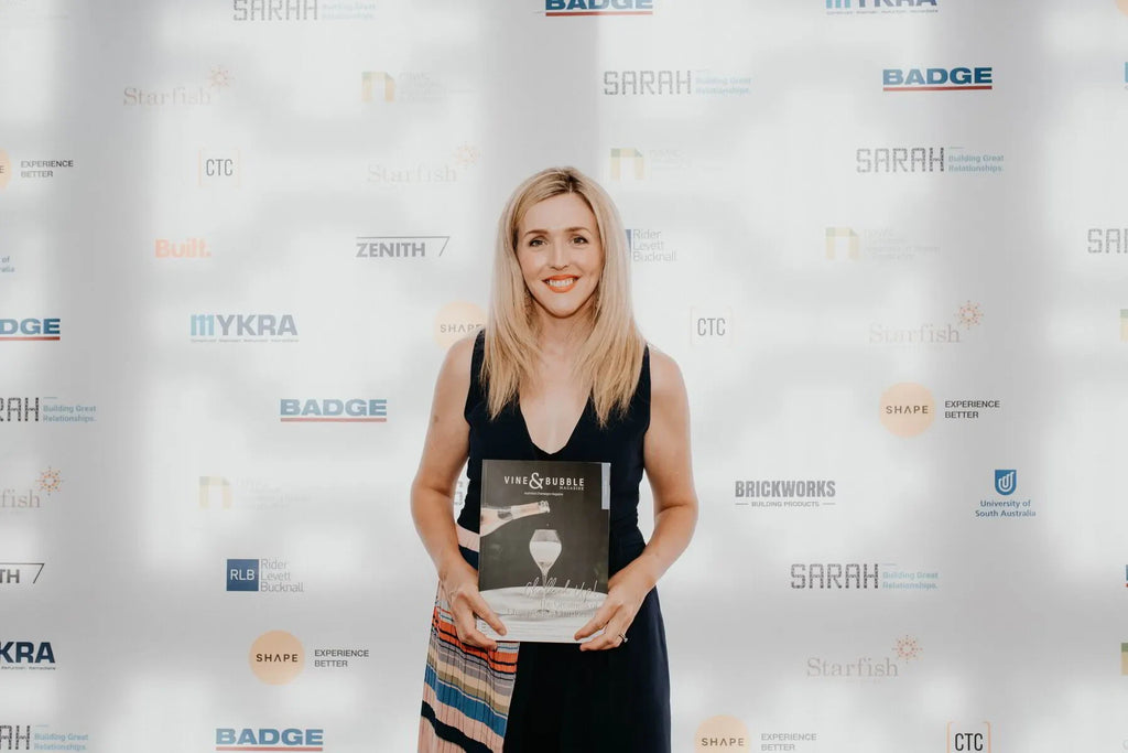 Smiling woman holding Vine & Bubble magazine at awards event with branded backdrop