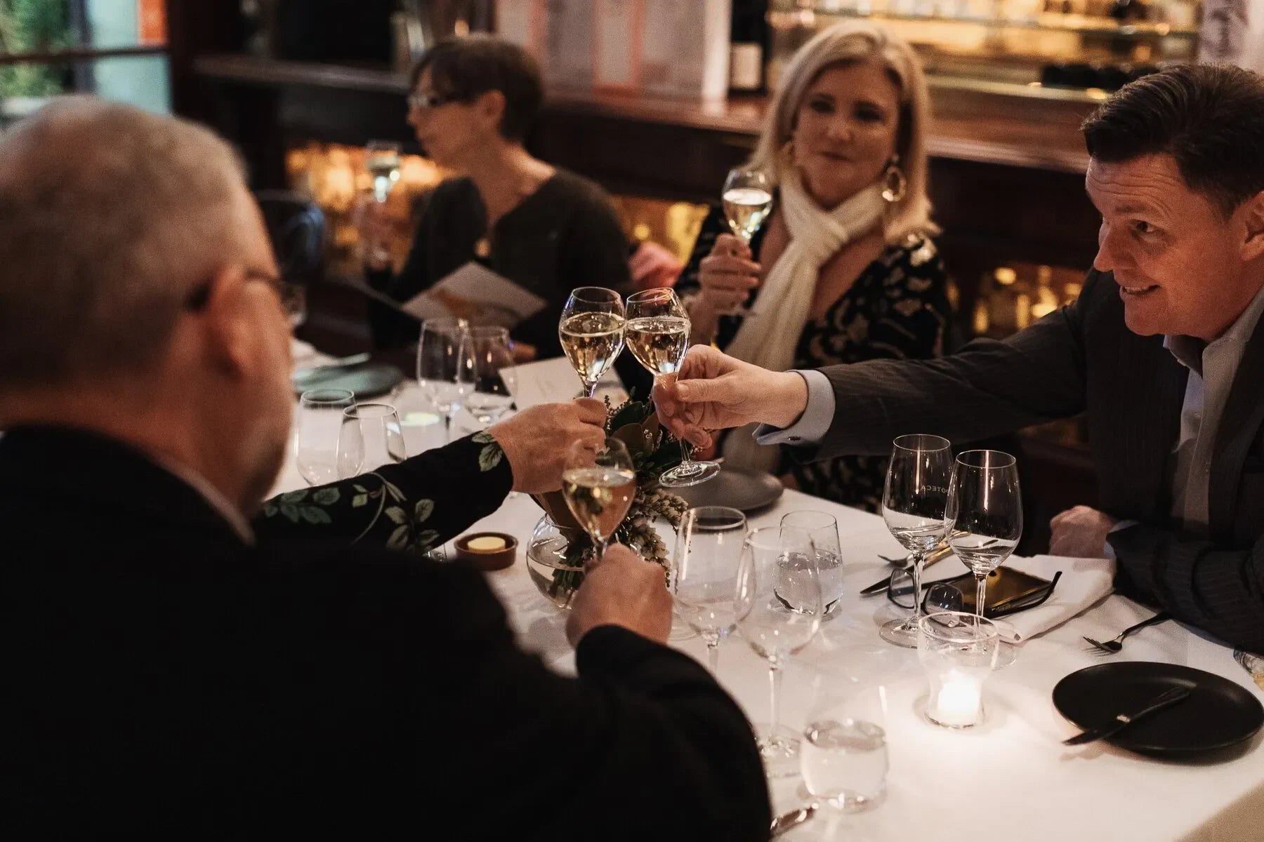 Elegant dinner party with four adults toasting champagne at a candlelit restaurant table