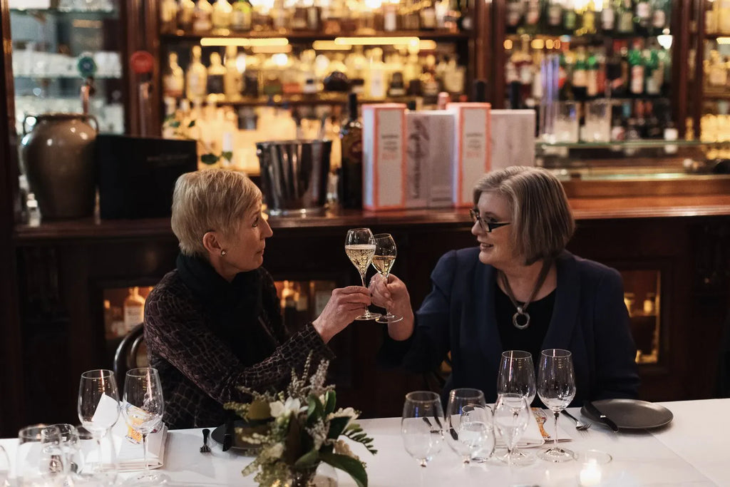 Two women toasting champagne at elegant dinner table in upscale bar setting