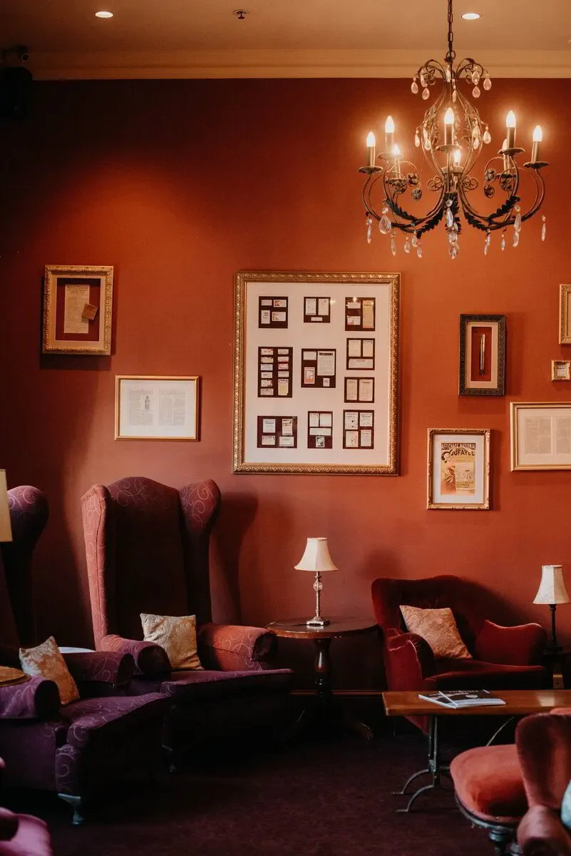 Elegant lounge with velvet armchairs, framed art on red walls, vintage chandelier, cozy decor