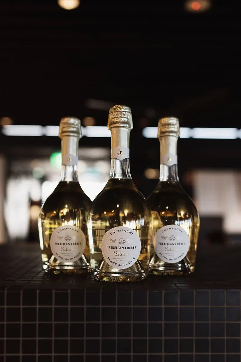 Three Frerejean Frères Soleil Blanc de Blancs champagne bottles on a dark tiled surface