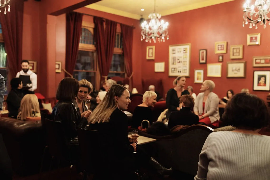 Elegant lounge with people socializing, red walls, chandeliers, and framed art decor