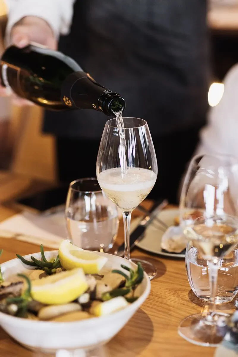 Champagne being poured into a wine glass at an elegant dining table with lemon seafood dish