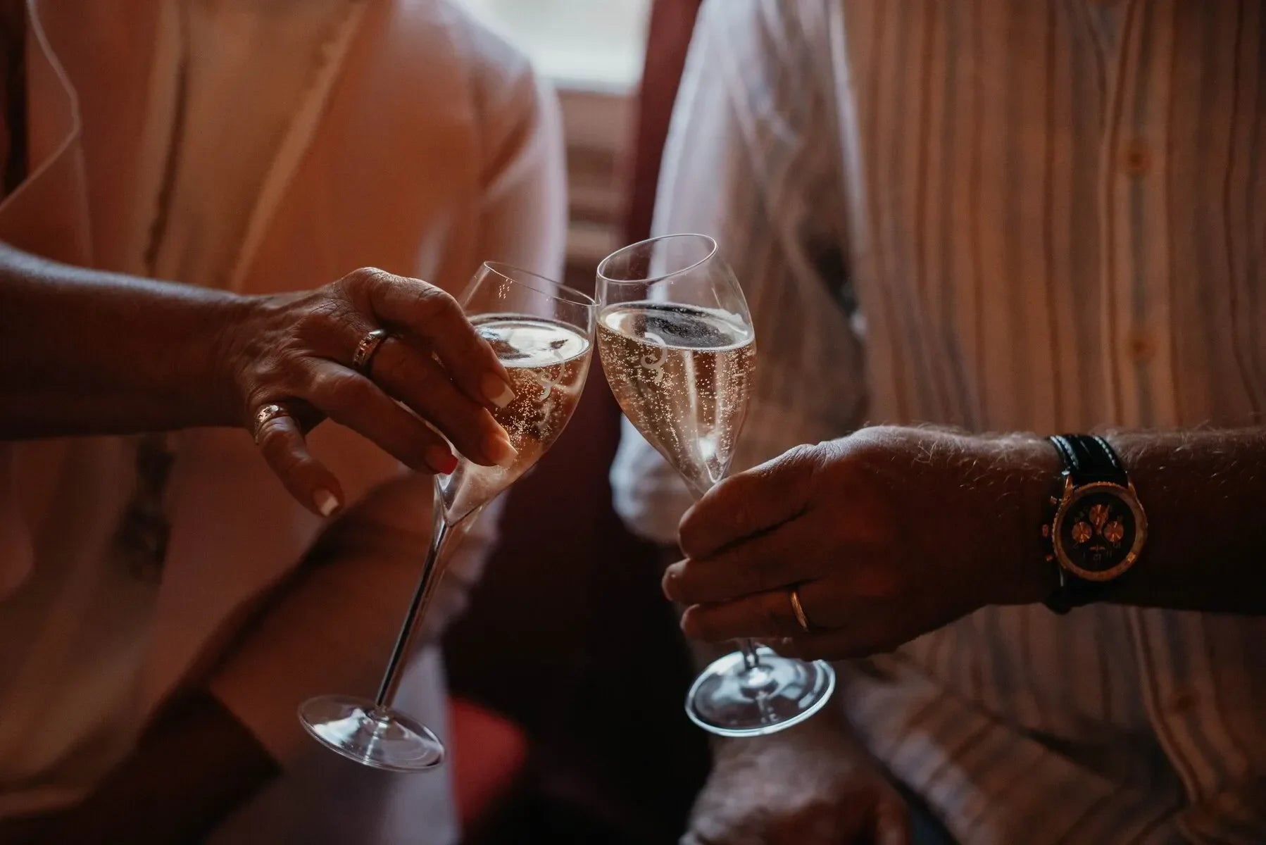 Two people clinking champagne glasses in a warm, celebratory indoor setting