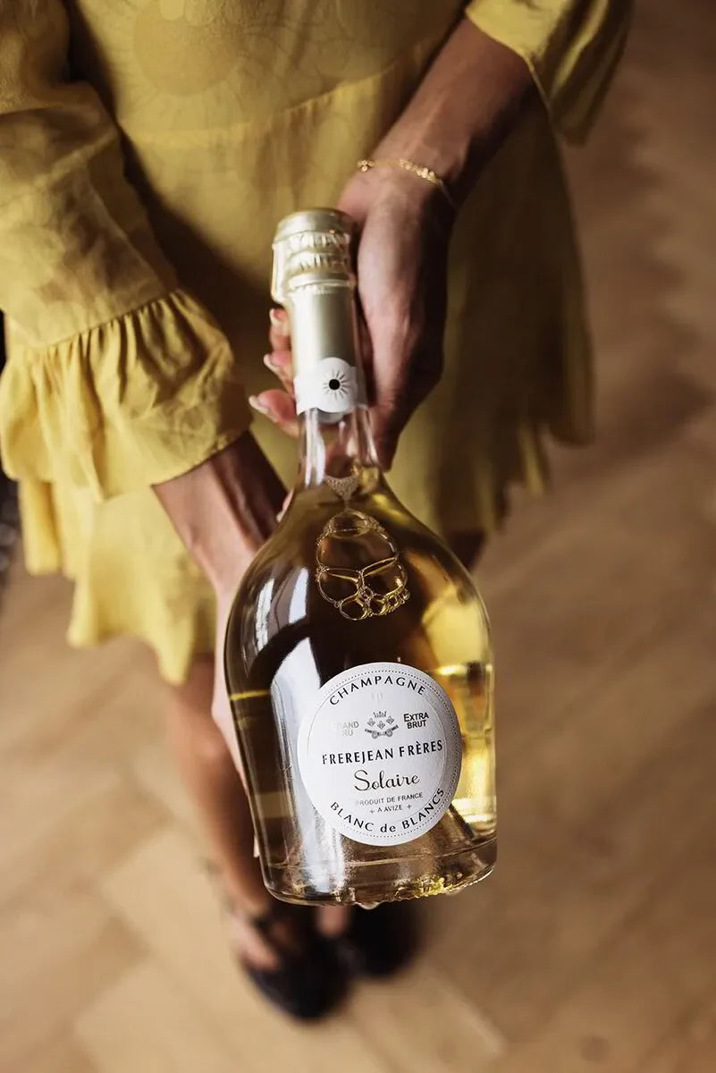 Woman in yellow dress holding Frerejean Frères Solaire Blanc de Blancs champagne bottle