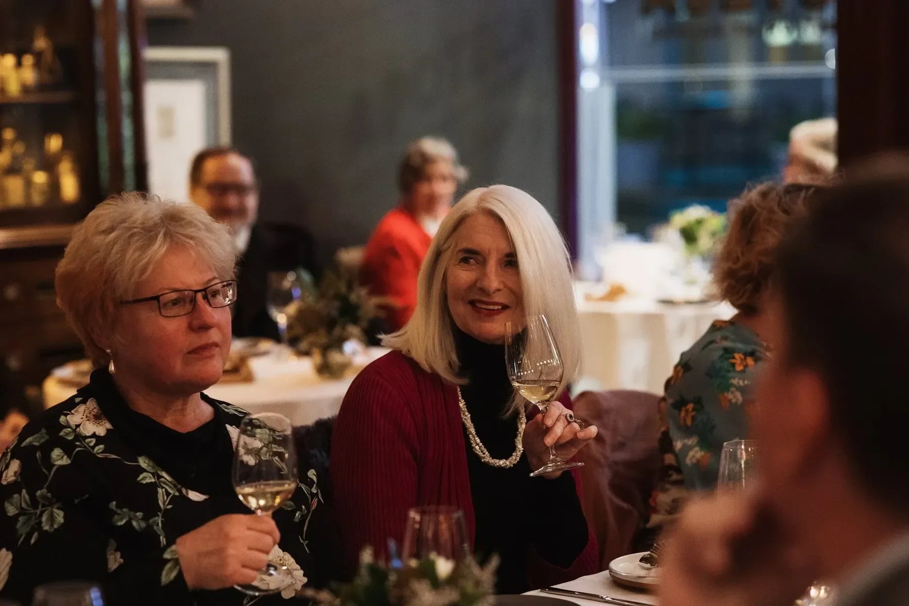 Women enjoying white wine at an elegant dinner party in a cozy restaurant setting
