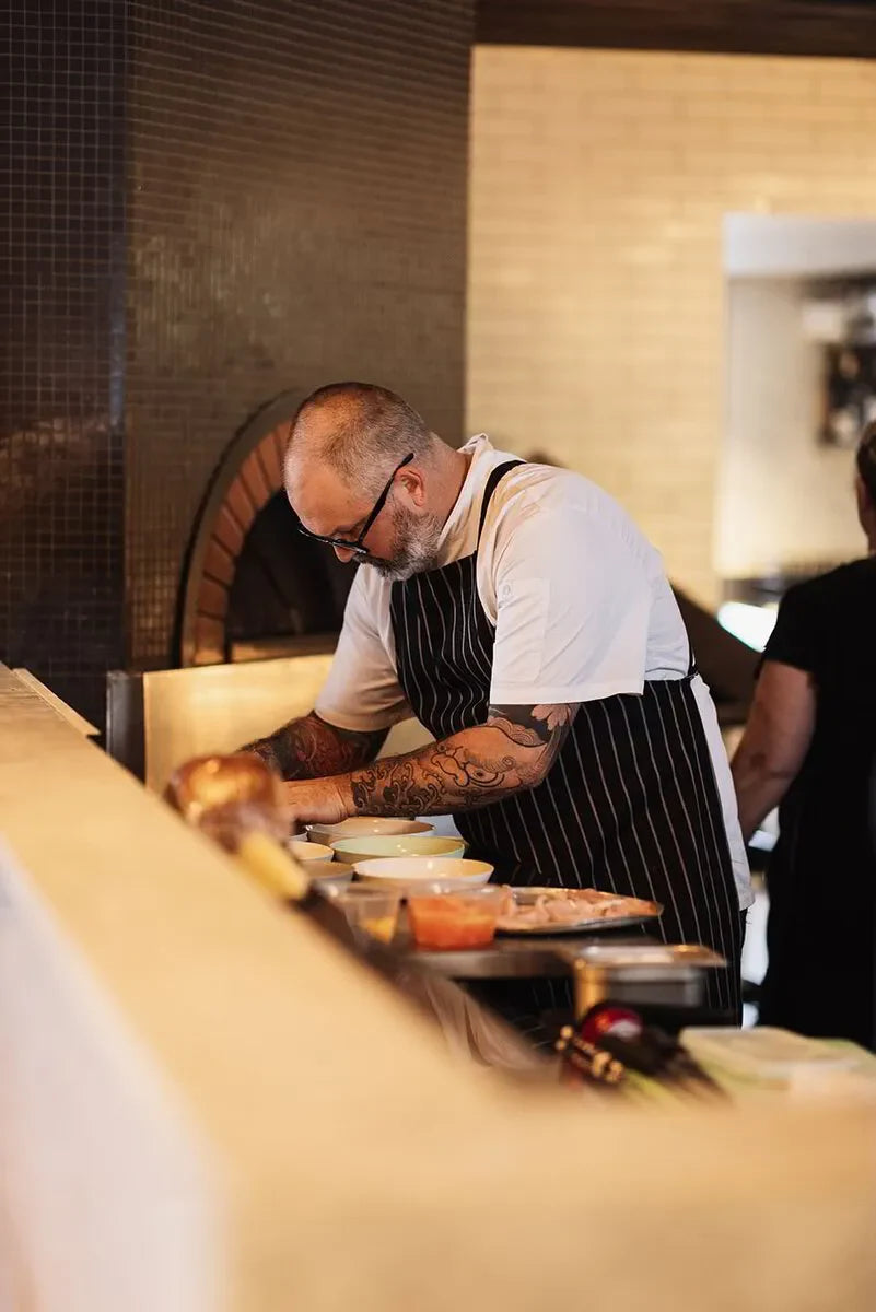 Tattooed chef in striped apron preparing food in modern restaurant kitchen