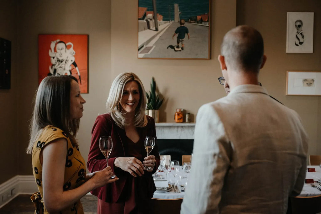 Group of adults socializing with wine glasses at indoor dinner party, art on walls