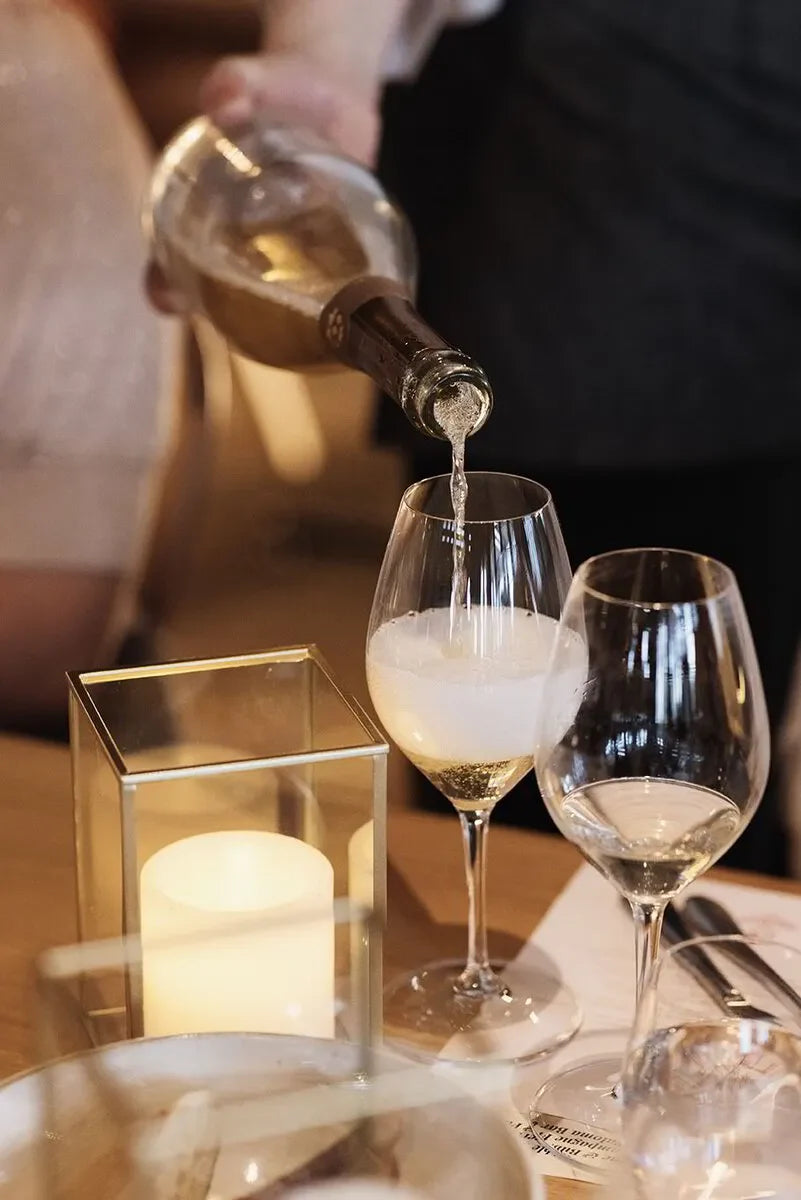 White wine being poured into glass at elegant dinner table with candlelight