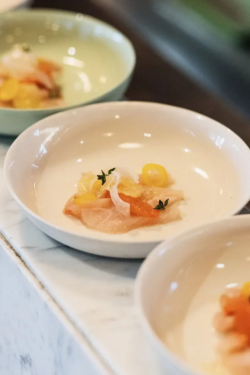 Gourmet appetizer with thinly sliced fish, citrus, and herbs in a white bowl on marble counter