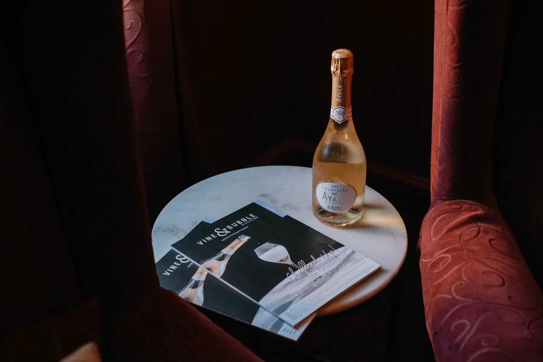 Bottle of Ayala Champagne and Vine & Bubble magazines on a round marble table