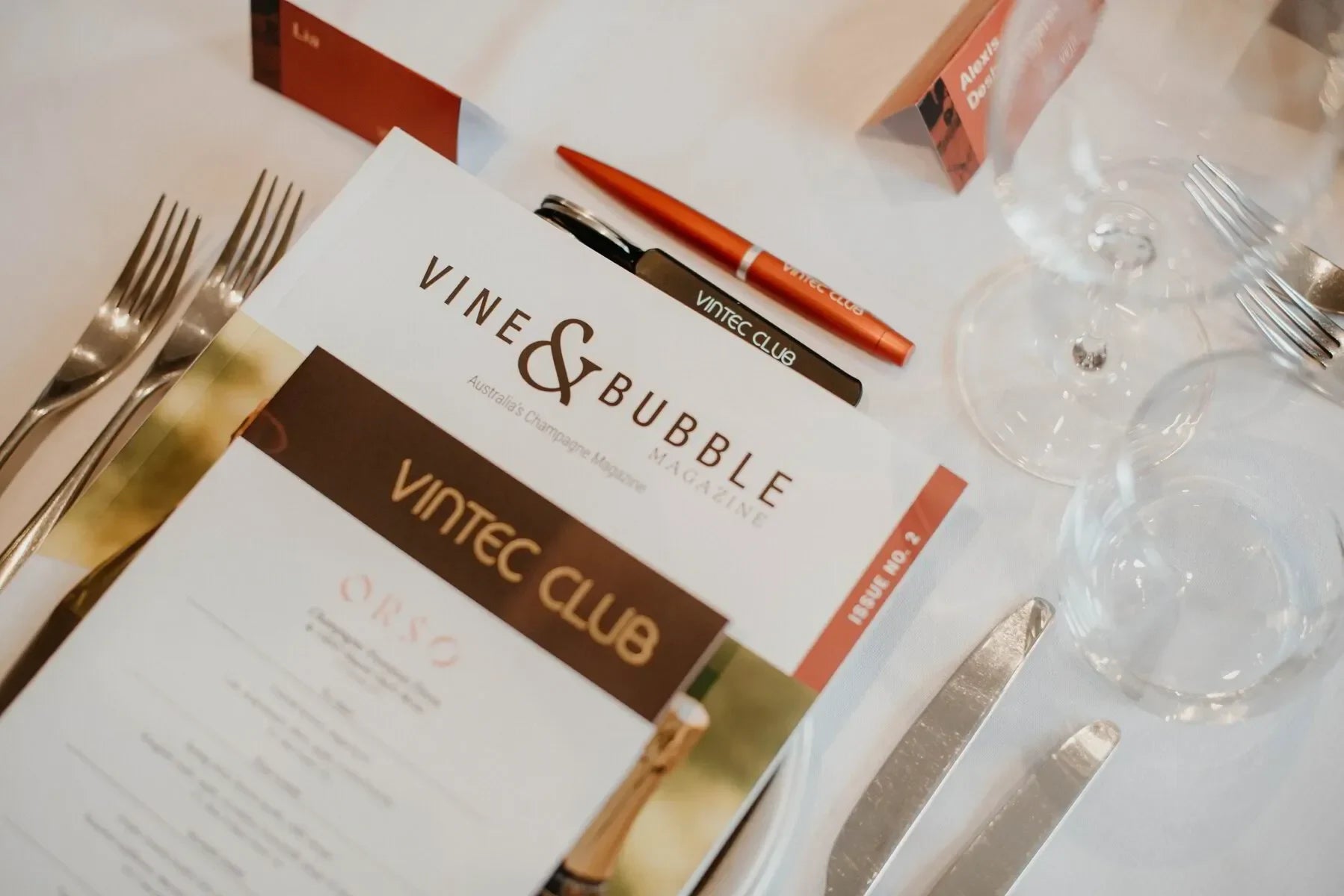 Vintec Club event table setting with Vine & Bubble magazine, cutlery, wine glasses, and pen